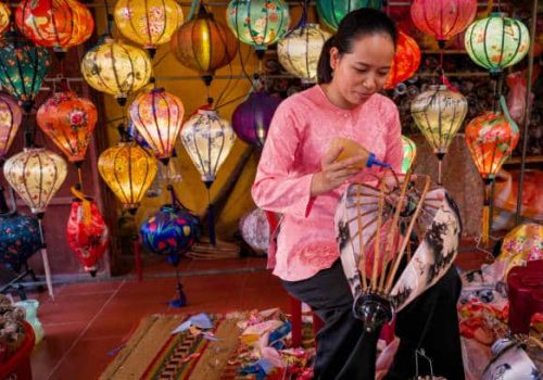 Vietnamese woman making traditional silk hanging lanterns, night market in Hoi An. Hoi An is situated on the east coast of Vietnam. Its old town is a UNESCO World Heritage Site because of its historical buildings.